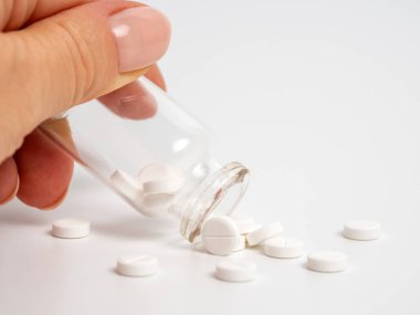 Beyaz arka planda cam şişeden beyaz hapları sallayan kadına yakın durun. İlaç veya antidepresanlarla tıbbi tedavi kavramı, sağlık hizmetleri veya uyuşturucu bağımlılığı.