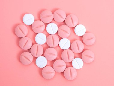 Pembe arka planda pembe ve beyaz haplar yığını. İlaçlar, vitaminler veya tabletlerdeki besin takviyeleri ile tıbbi tedavi. Kadın sağlığında doğum kontrol hapları..