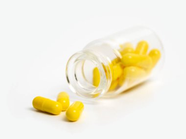 Sarı haplar, beyaz arka planda açık duran cam şişenin yanında. Tıbbi tedavi kavramı kapsüller, sağlık hizmetleri veya uyuşturucu bağımlılığına ilişkin vitaminler veya takviyeler.
