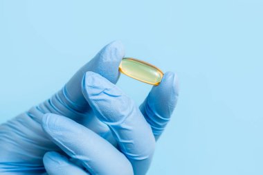 Doktor, eczacı ya da bilim adamı omega 3 kapsülü tutan mavi eldiveni teslim etti. Mavi arka planda vitamin hapı ya da takviye. Sağlık ve bilimsel araştırmalar. Yaklaş, seçici odaklanma.