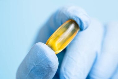 Doktor, eczacı ya da bilim adamı omega 3 kapsülü tutan mavi eldiveni teslim etti. Mavi arka planda vitamin hapı ya da takviye. Sağlık ve bilimsel araştırmalar. Yaklaş, seçici odaklanma.