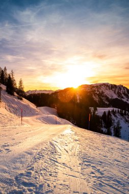 İsviçre Alpleri 'ndeki Klewenalp Dağı' nda kış manzarası. Gün batımında. Popüler kayak yamacı ve karlı dağların, köknar ağaçlarının ve batan güneşin olduğu kış sporları. Dikey yönelim.