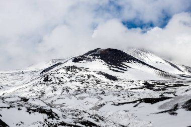 İtalya 'nın Sicilya adasındaki Etna Dağı volkanı krateri. Siyah volkanik lav taşlı Silvestri kraterlerinin manzarası. Mavi gökyüzü, bulutlar ve dumanla kaplı aktif volkan yamaçları.