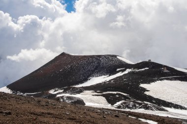 İtalya 'nın Sicilya adasındaki Etna Dağı volkanı krateri. Siyah volkanik lav taşlı Silvestri kraterlerinin manzarası. Mavi gökyüzü, bulutlar ve dumanla kaplı aktif volkan yamaçları.