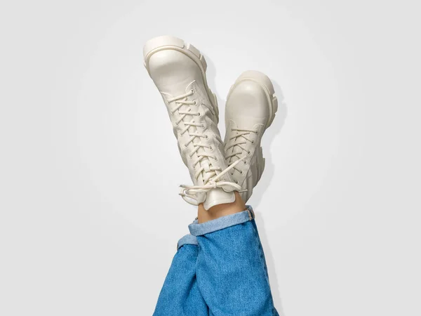 Crossed female legs in white combat boots and blue jeans upside down on white background, side view. Woman wearing trendy military beige shoes on high platform with laces. Seasonal female fashion.