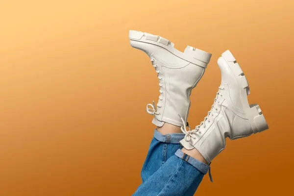 Female legs in white combat boots and blue jeans upside down on orange background, side view. Woman wearing trendy military beige shoes on high platform with laces. Seasonal female fashion.