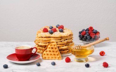 Bir yığın Belçika waffle 'ı, böğürtlen, bal ve kırmızı kahve. Mermer masada nefis bir yaz kahvaltısı. Kalp şeklinde waffle ve ahududu ve yabanmersini karışımı..