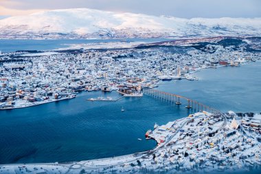 Tromso, Norveç 'in Storsteinen Dağı' ndan kış manzarası. Tromsoya adası, Tromso şehir merkezi, liman, Fiyort üzerindeki Sandnessundet Köprüsü ve arka plandaki dağlarla karlı çatılar..