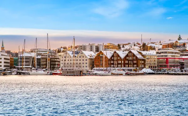 Tromso limanı kışın gün batımında, Norveç. Tromso limanındaki İskandinav binaları ve tekneleri. Norveç 'in kuzeyindeki Kuzey Kutup Dairesi kasabasında karlı kış manzarası.