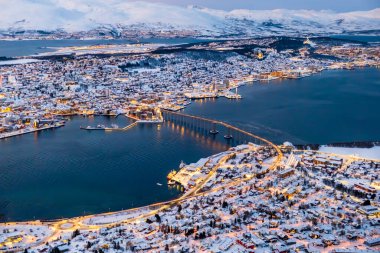 Tromso, Norveç 'in havadan görünüşü, Storsteinen dağından kışın şehrin ışıkları. Tromsoya adasının karlı çatıları Tromso kasabası, limanı, Fiyort üzerindeki Sandnessundet köprüsü ve arka planında dağlar