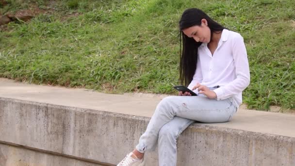 Латинська Жінка Використовує Мобільний Телефон Сидячи Відкритому Повітрі — стокове відео