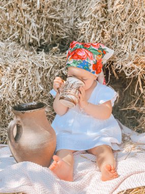 Beyaz şapkalı küçük kız çimenlerde oturur ve bir sürahi yer..