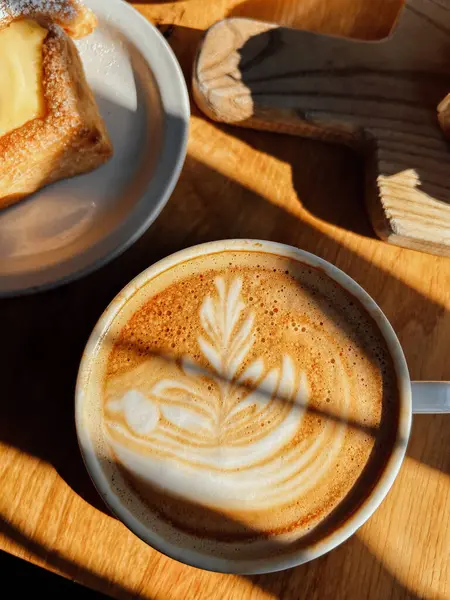 Bir fincan sıcak cappuccino ve gün ışığında masada latte sanatı..