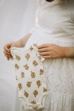 Beyaz arka planda bebek kıyafetleriyle beyaz ayı oyuncağı tutan bir bebek. Bebek kıyafetleri..