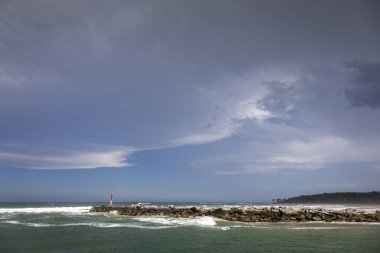 Big rocks and ominous storm clouds in sky over water at breakwall on Wooli Wooli River clipart