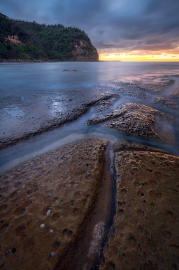 sunset over rocks and long exposure water at Little Beach on NSW Central Coast Australia clipart