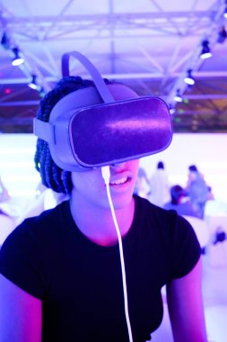 Örgü ören, sanal gerçeklik gözlüklü, neon ışıklı arka planı dikey bir kız.