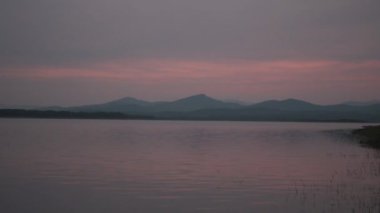 Bataklıkta gün batımı, arka planda dağlar, altın saat, yatay turkuaz tonlar.