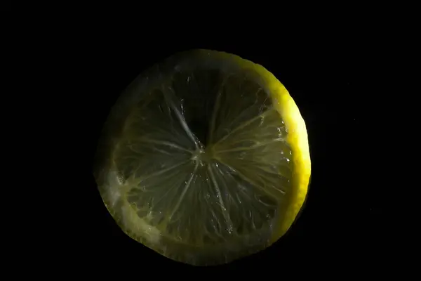 Fresh slice of yellow lemon with black background and reflection horizontally with ray of light