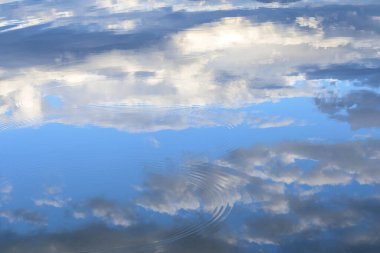 Dalgalı suda mavi gökyüzü olan beyaz bulutların yansıması.