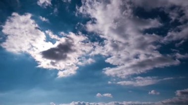 Mavi gökyüzünde, parlak güneşin altında hareket eden bulutlar, zaman kavramı. Bulutuzay arkaplanı. Muhteşem cennette hafif kabarık bulutların zamanı. Manzaralı atmosfer. Hava değişikliği. Doğa. 4K