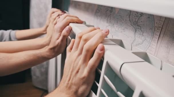 カップルは壁によって暖房ラジエーターの手を暖める 冷凍男性と女性の手は 家庭用加熱バッテリーに触れ 暖かくしようとします 寒い季節に家を加熱する問題 暖房設備が悪い — ストック動画