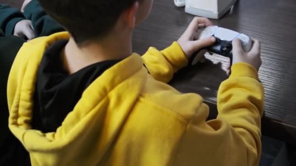 ゲーム機でゲーマー 十代の若者はテーブルに座っている間 彼の手のジョイスティックを制御します クローズアップ エンターテイメントセンターのゲームゾーンでビデオゲームコントローラーを使用して男の子 ゲーマーの再生ビデオ — ストック動画