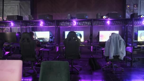 青少年朋友在电脑俱乐部玩网络游戏 坐在计算机椅子上的男孩们 带着耳机 在电脑上玩射击游戏 在有霓虹灯的俱乐部游戏室里玩的游戏者 — 图库视频影像