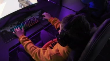 Esport kulübündeki genç bir çocuk oyun sandalyesinde monitörün önünde oturup atış oyunu oynuyor. Bilgisayar kulübünde kulaklık takan bir genç bir video oyununa odaklanıyor, arkadaşlar çevrimiçi turnuva oynuyor