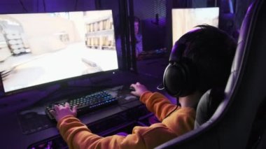 Esport kulübündeki genç bir çocuk oyun sandalyesinde monitörün önünde oturup atış oyunu oynuyor. Bilgisayar kulübünde kulaklık takan bir genç bir video oyununa odaklanıyor, arkadaşlar çevrimiçi turnuva oynuyor