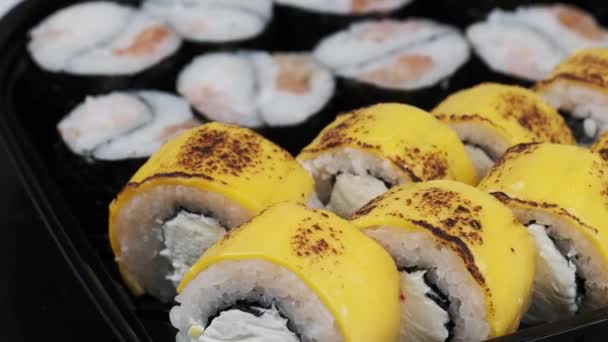 寿司卷在塑料盒中旋转 新鲜的日本寿司 配上费城奶酪 鲑鱼片 鳄梨和黄瓜 寿司装在塑料容器内 外卖食品 — 图库视频影像