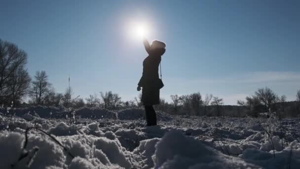 在冬日的景色下 女人把智能手机举起来挡住阳光 试图捕捉手机信号 年轻姑娘的侧影举着电话向太阳伸出手来 搜索信号 没有连接 — 图库视频影像