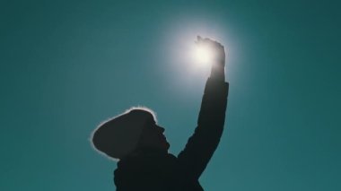 Güneşe karşı olan genç kadın, kışın kaybolan cep telefonu sinyallerini yakalamak için elini kaldırıyor. Akıllı telefon güneşi kapatır. Doğada iletişim zayıf, sinyal yok, mobil internet sinyali yok.
