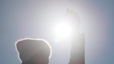 Kadın kış manzarasında akıllı telefonunu güneşe doğru tutarak cep telefonunun sinyalini yakalamaya çalışıyor. Genç bir kızın silueti elinde telefonla güneşe uzanıyor. Arama sinyali, bağlantı yok.