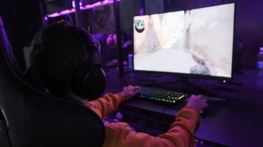 Esport kulübündeki genç bir çocuk oyun sandalyesinde monitörün önünde oturup atış oyunu oynuyor. Bilgisayar kulübünde kulaklık takan bir genç bir video oyununa odaklanıyor, arkadaşlar çevrimiçi turnuva oynuyor