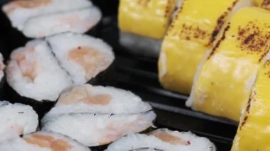 Japon suşi ruloları plastik kutuda dönüyor, yakın plan. Zencefilli, wasabi ve soya soslu taze suşi. Philadelphia peynirli suşi, nori, yengeç çubuğu, somon filetosu ve salatalık.