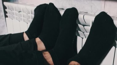 Donmuş çoraplar duvarın yanındaki ısıtıcı kaloriferde ısıtılır. Erkek ve dişi bacakları ev ısıtma bataryasına dokunup ısınmaya çalışır. Dairede soğuk, kötü ısıtma sistemi, soğuk mevsim