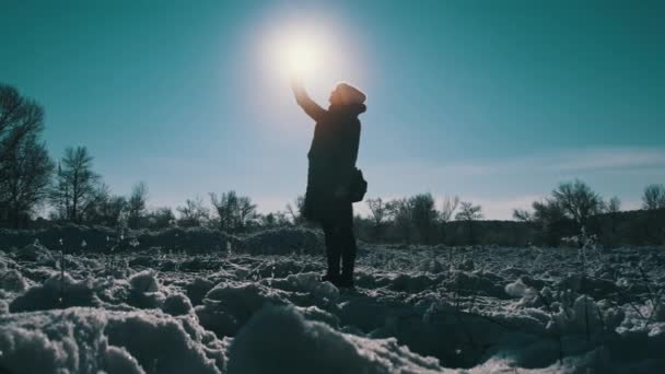 年轻女子抵御阳光时 高高地举起手 试图在冬季捕捉丢失的手机信号 智能手机遮住了太阳 通信不良 没有信号 没有移动因特网搜索信号 — 图库视频影像