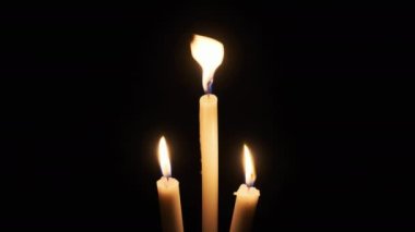 Siyah arka planda üç mum yanığı. Yanıp sönen mumların sarı alevi karanlığı aydınlatıyor, yakından. İzole edilmiş, kopyalanmış. Anma, din, kutlama kavramları. Mum alevi sallanıyor