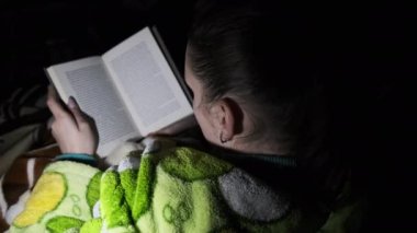 Bir kadın, geceleri bir el fenerinin ışığında kanepede yatan bir kitap okur. Sabahlık ve rahat bir oda giymiş bir kız kitap okumakla meşgul. Sıcak, sıcak bir oturma odasında fener ışığının tadını çıkarıyorum..