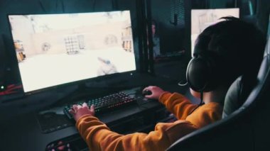 Bilgisayar kulübündeki bir çocuk oyun sandalyesinde oturup atış oyunu oynuyor. Esport Siber Kulübü 'nde kulaklık takan ve neon ışıkları video oyununa odaklanan bir genç. E-spor, hobi, sanal turnuva