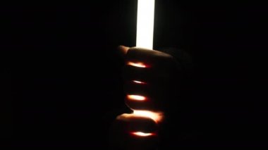 Erkeklerin elleri siyah arka planda hafif bir kılıç tutar. Erkek parmakları uzun, parlak bir LED boru feneri tutar. Neon ışın kılıcı. El fenerinden el silueti. 4K