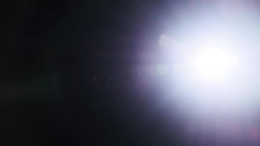 El fenerinin ışığı siyah bir arkaplanda kameraya yansıyor. Parlak ışığın kamera lensine yansımasının ışık efekti. Mavi Dijital Lens Fişeği, Soyut Örtüler Arkaplan. 4K