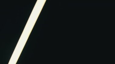 Neon LED kılıcı siyah arka planda sağa sola hareket eder. Tüplü fenerin parlak beyaz ışığı. Video geçiş efekti, geçiş. Parlak neon ışığı, soyut floresan arka plan. 4K