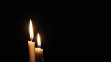 Siyah arka planda iki mum yakılıyor, yakın plan. Sarı yanıp sönen alev karanlığı aydınlatıyor. Ateşin sıcak parıltısı geceleri yanıyor ve rüzgarla hareket ediyor. İzole edilmiş, kopyalanmış. 4K