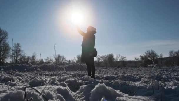 在冬日的景色下 女人把智能手机举起来挡住阳光 试图捕捉手机信号 年轻姑娘的侧影举着电话向太阳伸出手来 搜索信号 没有连接 — 图库视频影像