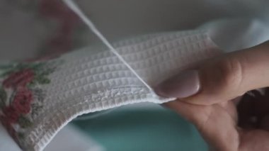 Genç kadın elleri yavaş çekimde iplik ve iğneyle elle dikilir, yakın çekimde. Manikürlü kadın parmakları evde günlük kıyafetlerle otururken dikiş dikiyor. Sıcak atmosfer, yaşam tarzı, el yapımı.
