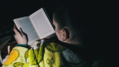 Baygınlık sırasında fener ışığında kitap okuyan bir kadın. Rahat bir odada, kanepede uzanmış sabahlık giymiş bir kadın geceleri kitap okumakla meşgul. Oturma odasındaki kitabın tadını çıkarıyorum..