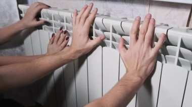 Donmuş erkek ve kadın elleri radyatöre dokunup ısınmaya çalışıyor. Ev ısıtma problemi. Soğuk mevsim konsepti sırasında ev sıcaklığı. Elleri ısıtma pili ile ısıtılır. Apartman soğuk.