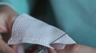Güzel kadın elleri iplik ve iğneyle elle dikilmiş. Genç bir kadın rahat bir kanepede ev kıyafetleri içinde otururken dikiş diker. Ev atmosferi ve pencereden gelen güneş ışığı. Yaşam tarzı, el yapımı. 4K